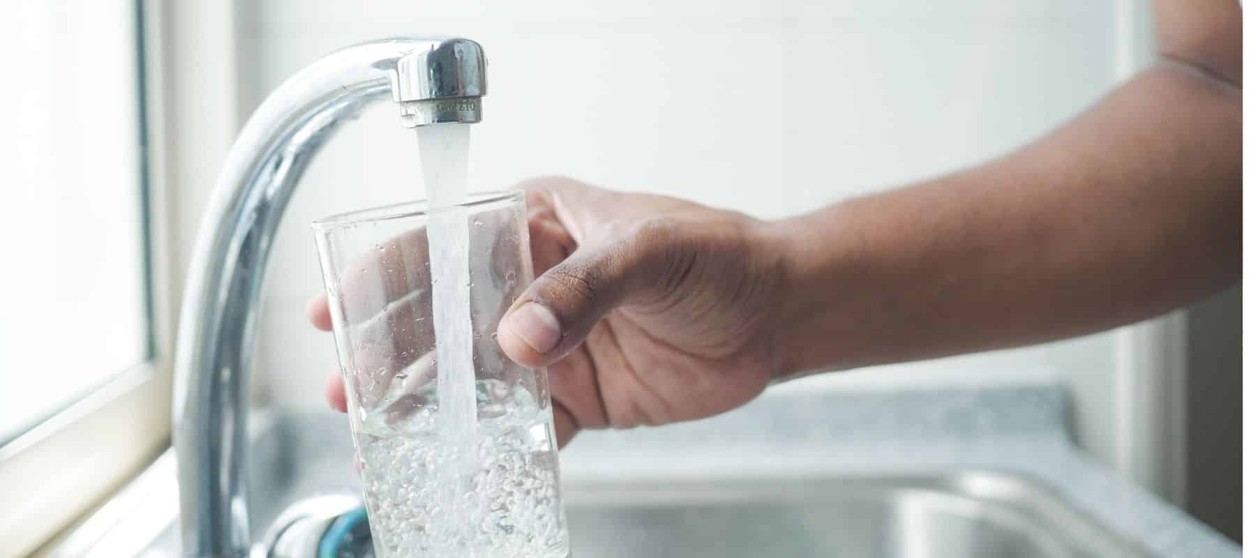 person filling up a glass of water from the tap