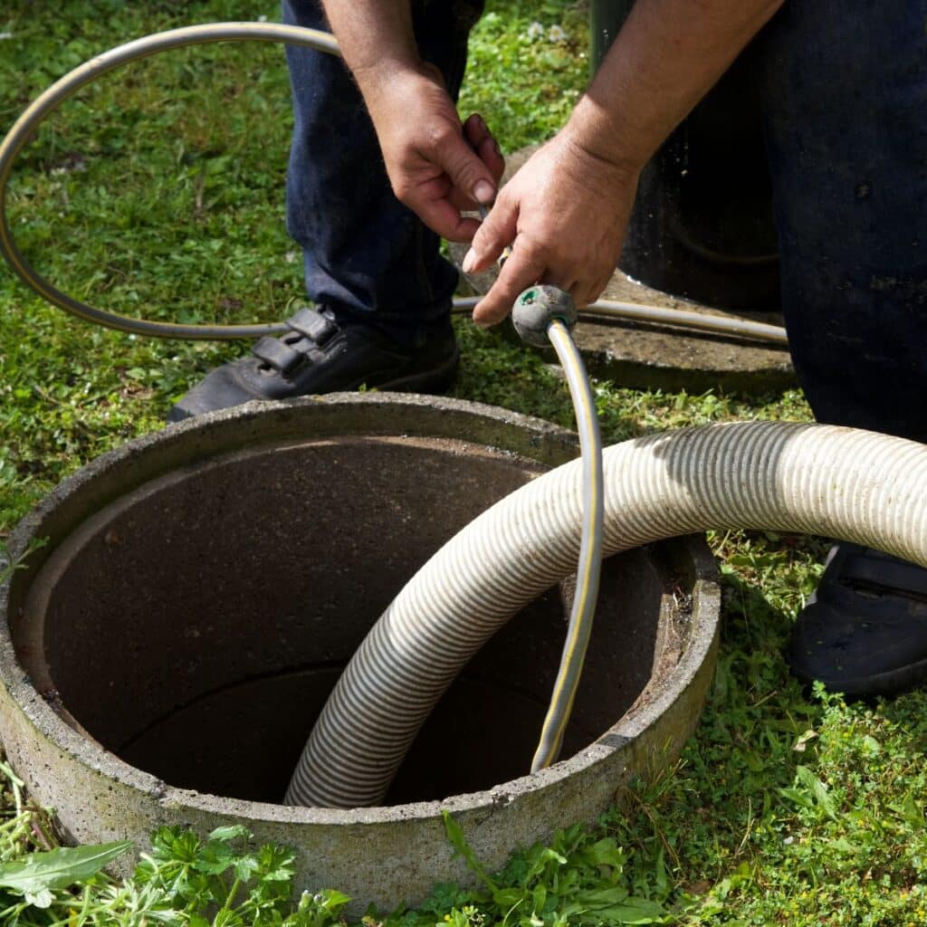 man using a hose to clean an outdoor drain