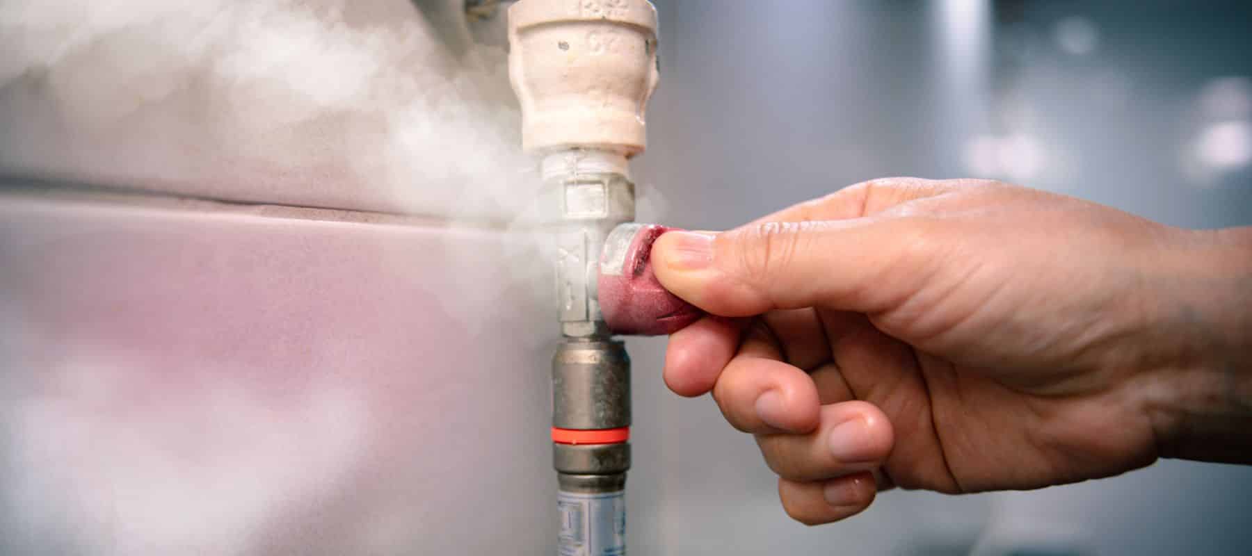 closeup of a gas line depicting gas leaking out of the line and a hand trying to turn off the line